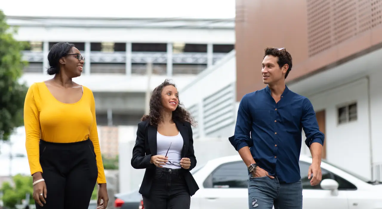 Trois personnes souriantes marchent ensemble à l’extérieur en discutant.