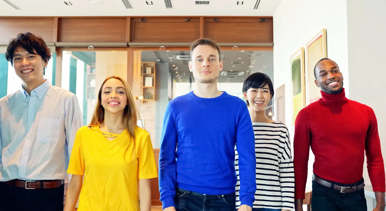 ਵੱਖ-ਵੱਖ ਪਿਛੋਕੜਾਂ ਦੇ ਨੌਜਵਾਨਾਂ ਦਾ ਸਮੂਹ ਅੰਦਰ ਇਕੱਠੇ ਖੜ੍ਹੇ, ਕੈਮਰੇ ਵੱਲ ਵਿਸ਼ਵਾਸ ਨਾਲ ਮੁਸਕਰਾਂਦੇ ਹੋਏ।