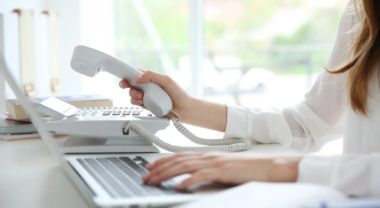 一個人拿著座機電話聽筒，同時在手提電腦上打字。