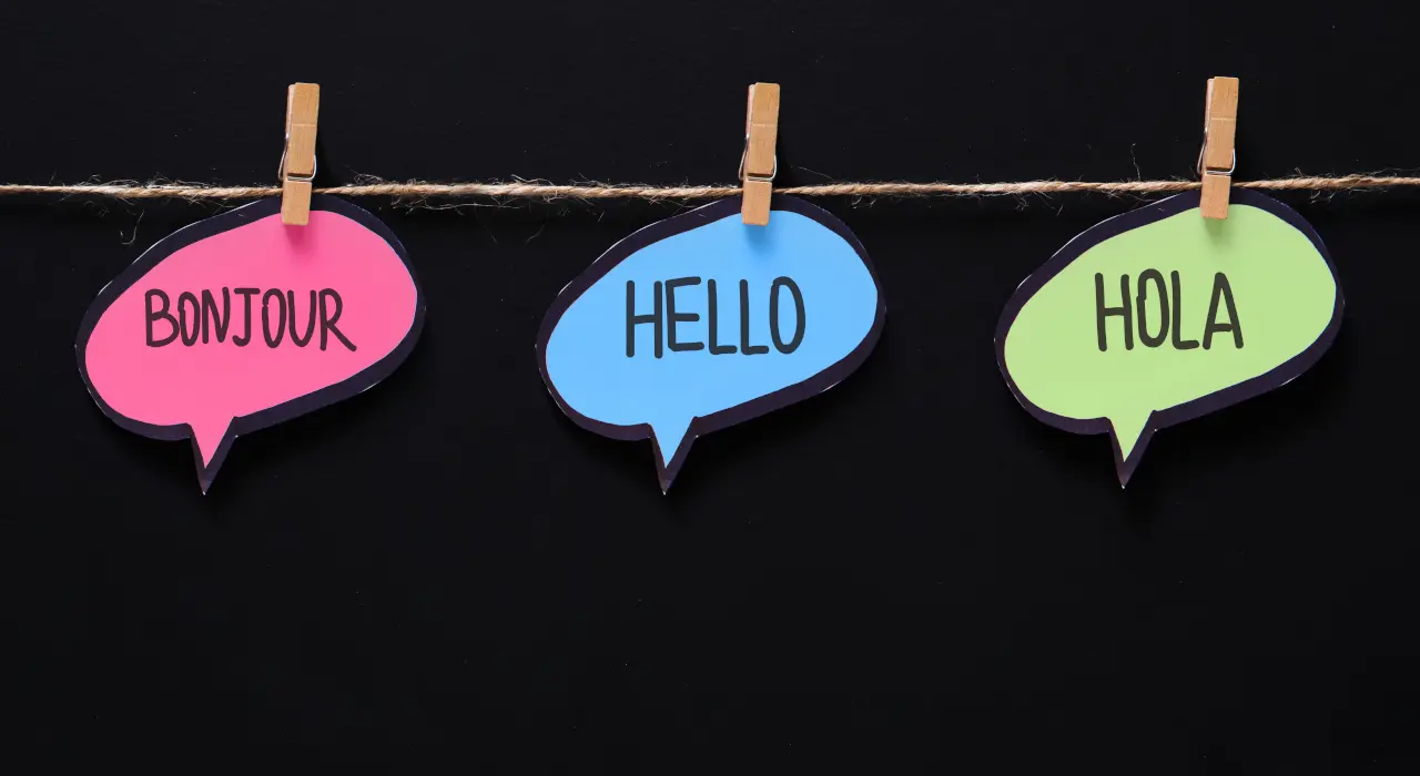 ਤਿੰਨ ਰੰਗੀਨ ਗੱਲਬਾਤ ਬੁੱਲਬਲੇ ਰੱਸੀ ਨਾਲ ਟੰਗੇ ਹੋਏ, ਜਿਨ੍ਹਾਂ ‘ਤੇ «BONJOUR», «HELLO» ਅਤੇ «HOLA» ਲਿਖਿਆ।