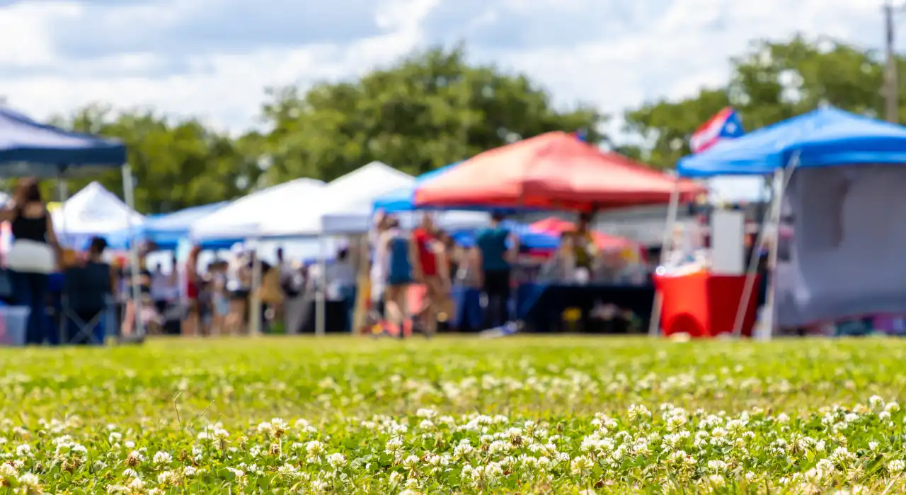 Outdoor festival with people walking among colourful tents and booths on a sunny day.