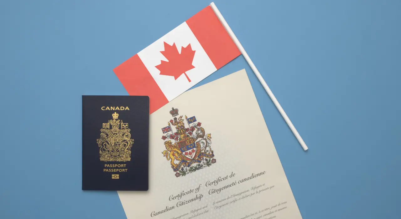 A Canadian passport, a certificate of citizenship, and a small Canadian flag placed on a blue background.