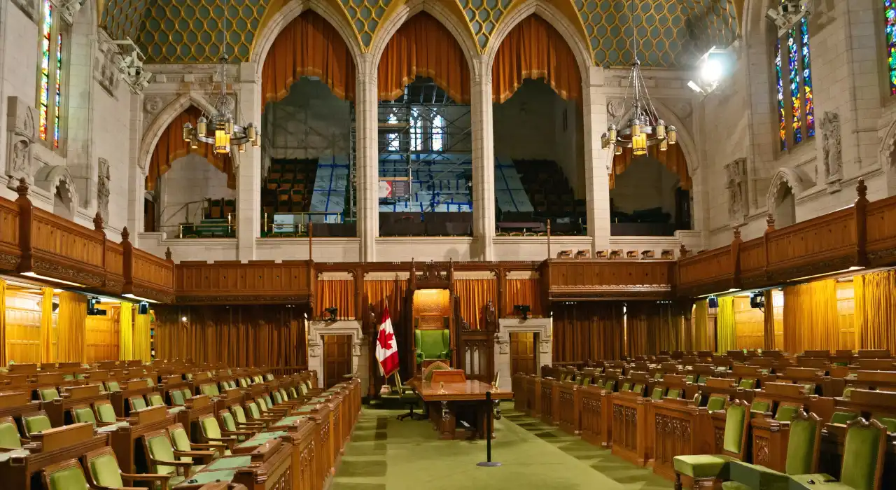 渥太華下議院議事廳內部景觀，綠色座椅、木製牆板和加拿大國旗。